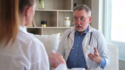 Senior Man Doctor Examining Yound Woman in Doctor Office or at Home Girl Patient and Doctor Have