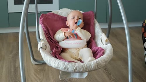 Adorable Infant Plays with Spoon in Swing Indoors