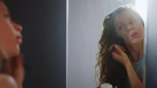Woman Applying Makeup with Brush in Bathroom Mirror