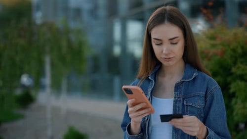 Woman Using Phone with Credit Card in City
