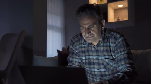 Man Using Laptop at Night in Dimly Lit Home