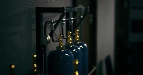 Gas Cylinders Arranged Neatly on a Metal Rack in a Shadowy Workshop