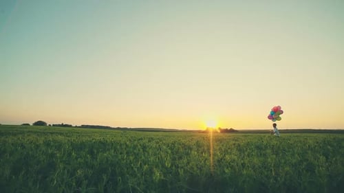 Child Runs with Balloons in Grassy Field at Sunset