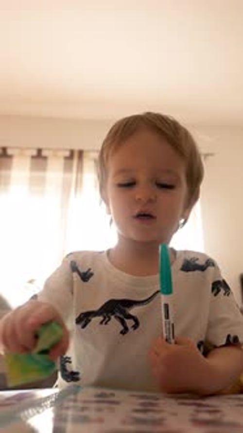 Vertical of Little Boy Sitting at Table With Toothbrush in Mouth