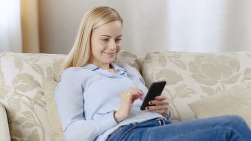 Woman with Blonde Hair Uses Smartphone on Sofa
