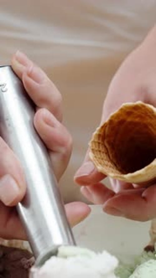 Vertikales Video. Nahaufnahme: Die Hände der Frau schöpfen Eisbällchen in die Waffeltüte
, indem sie