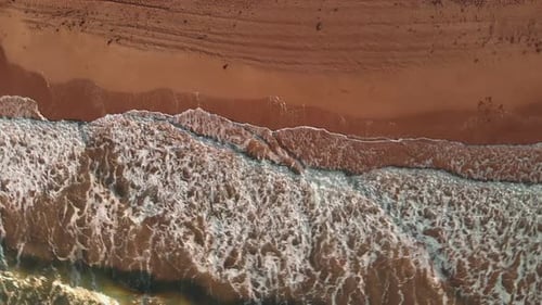 Huge sea waves crashing on sandy beach, splashing and creating white foam, top view.
