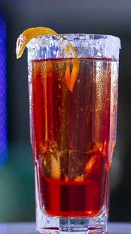 Little rotating table with red beverage. Beautiful cocktail with salt on glass top and orange peel
