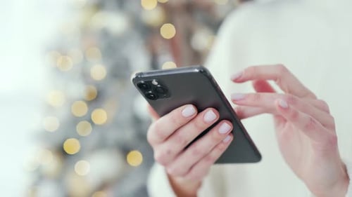Close up. Woman's hand holds a smartphone at home during winter New Year Xmas holidays. Female