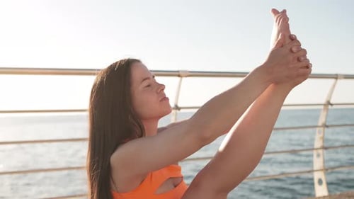 Young Woman in Orange Sports Wear Practicing Yoga on the Beach Above Sea at Amazing Sunrise