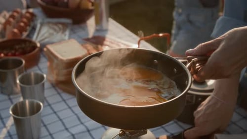 Hands of Woman Cooking Eggs with Bacon in Pan on Portable Stove at Campsite