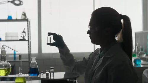 Research and Development of a Vaccine Dark Silhouette of a Female Scientist with a Glass Ampoule