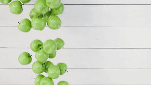 Green apples falling on white wooden background.