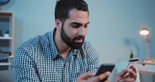 Man Using Phone and Credit Card Indoors