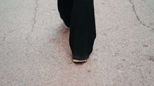 Rear View of a Feet Walking on the Street A Girl Wearing Dark Pants and Casual Leather Sneakers