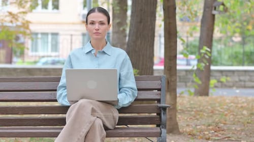 Woman Uses Laptop on Park Bench in Autumn