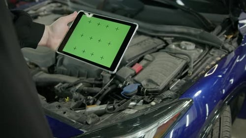 Male car service worker with a tablet in his hands on which there is a green screen near the hood