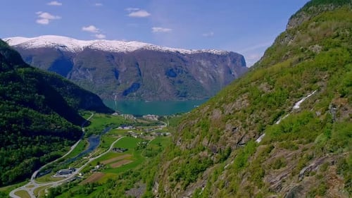 Hidden waterfall between the high green mountains with in the background the calm Aurlandsfjord. Bac