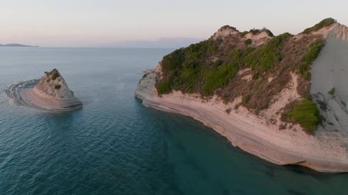 Aerial pan shot revealing a secluded sea stack next to the massive white cliffs of Cape Drastis