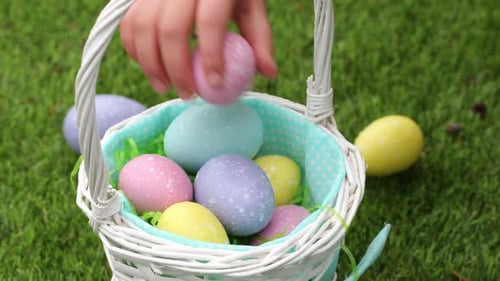 Kleines Mädchen legt im Frühlingsgarten vorsichtig bunte Ostereier in ihren Korb
