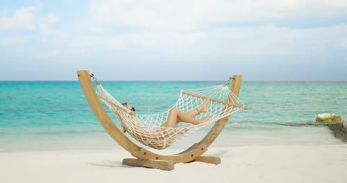 Idyllic Scene. Beautiful Woman Sunbathing Lying in Hammock on a Beach. Azure Beach with White Sands