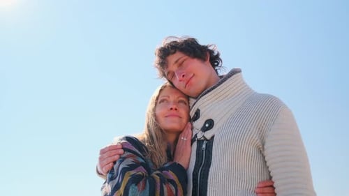 Man gently kisses smiling woman beneath clear spring sky in tender embrace.