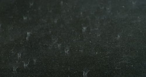 Ralentissement des gouttelettes de pluie sur le sol sombre, créant des formes d'éclaboussures abstraites