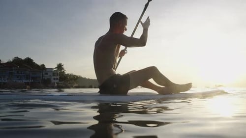 Man and Woman Paddleboarding at Sunrise on Tropical Sea