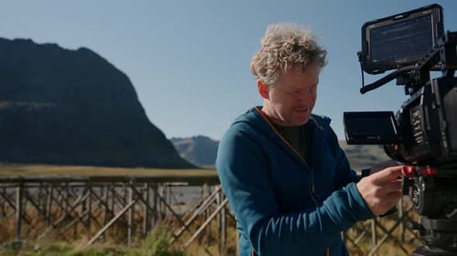 Man Adjusting Camera on Mountain Landscape