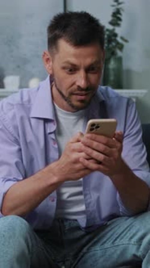 A Focused Man is Engaging with His Smartphone While Seated in His Modern Living Room Space