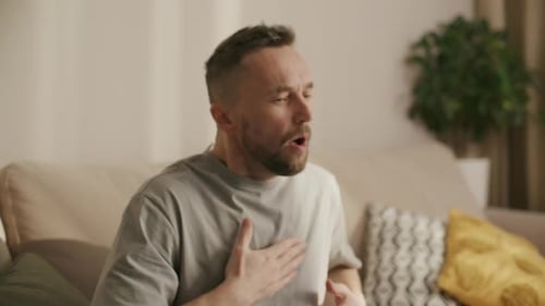 Man Coughing Holding Chest Sitting on Couch Indoors