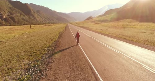 Flight Over Hitchhiker Tourist Walking on Asphalt Road Huge Rural Valley at Summer Day Backpack