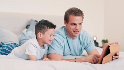 Father and Son Using Tablet on Bed Together
