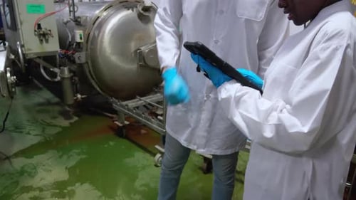 Un homme caucasien et une travailleuse afro-américaine portant une blouse de laboratoire vérifiant une tablette numérique.