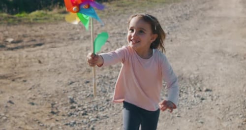 Girl Runs with Colorful Pinwheel Along Dirt Road