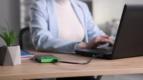 Mãos femininas digitando no teclado para transferir dados de um disco rígido portátil conectado a um computador