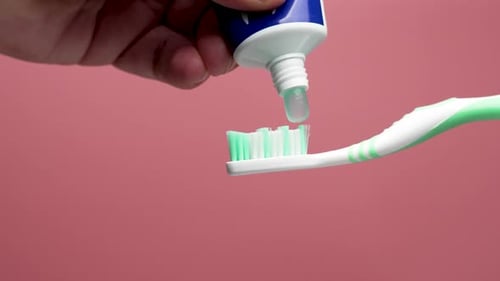 Toothpaste is applied to a toothbrush from a tube.