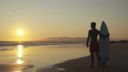 Surfer Silhouette with Surfboard at Golden Sunrise Beach