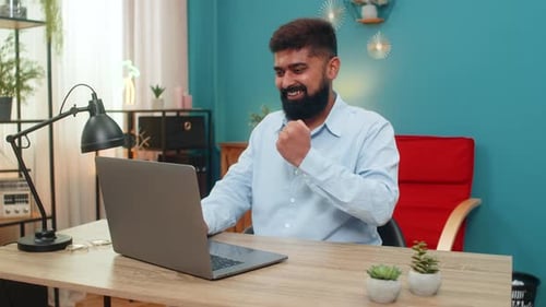 Man Works on Laptop, Celebrates Success in Home