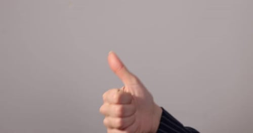 Woman Hand Giving a Thumbs Up Against Gray Background