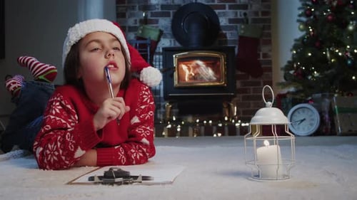 Очаровательный ребенок в шляпе Санты пишет рождественское письмо в уютной гостиной