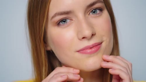Attractive young woman smiling gently touching her face posing in studio