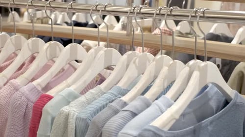 Female knitted sweaters hang on hangers in the store close-up.