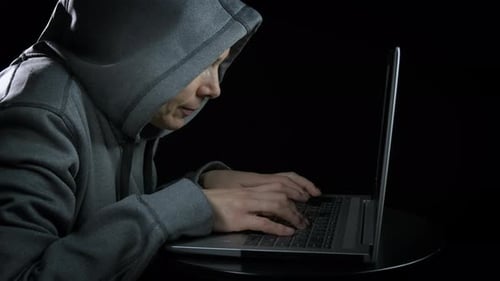 Hooded Figure Types on Laptop Keyboard at Night
