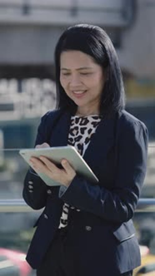 Positive Lady Manager Standing Outdoors and Using Tablet Making Notes Texting