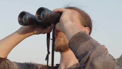 Portrait d'un homme charismatique avec une barbe et une moustache regardant le ciel à travers des jumelles