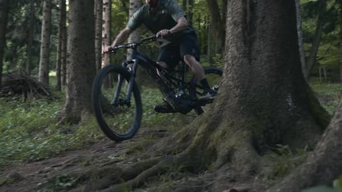 Young athletic man on MTB e-bike riding down the hill in a forest. Making a trick on one wheel.
