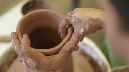 Over shoulder view of potter working wet clay rotating on workshop pottery wheel
