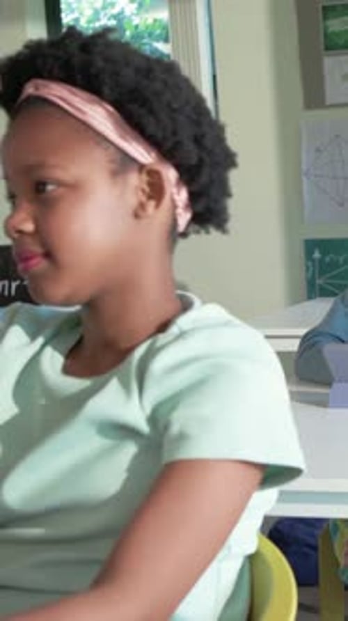 Girl raising hand to answer teacher question, raising then lowering and smiling with tablet, school