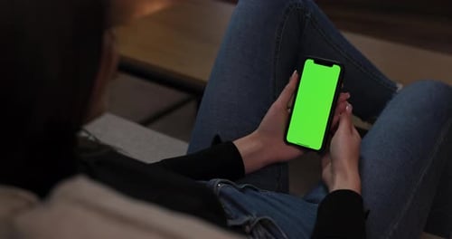 Woman Holds Smartphone with Green Screen Indoors